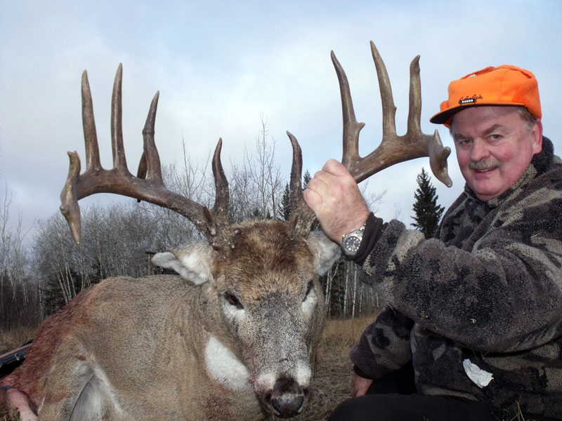 A hunter holding a dead deer by it's antlers.