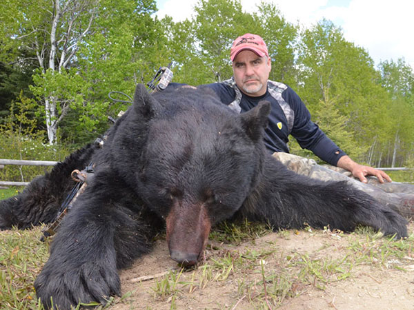 A hunter sitting next to a dead black bear.